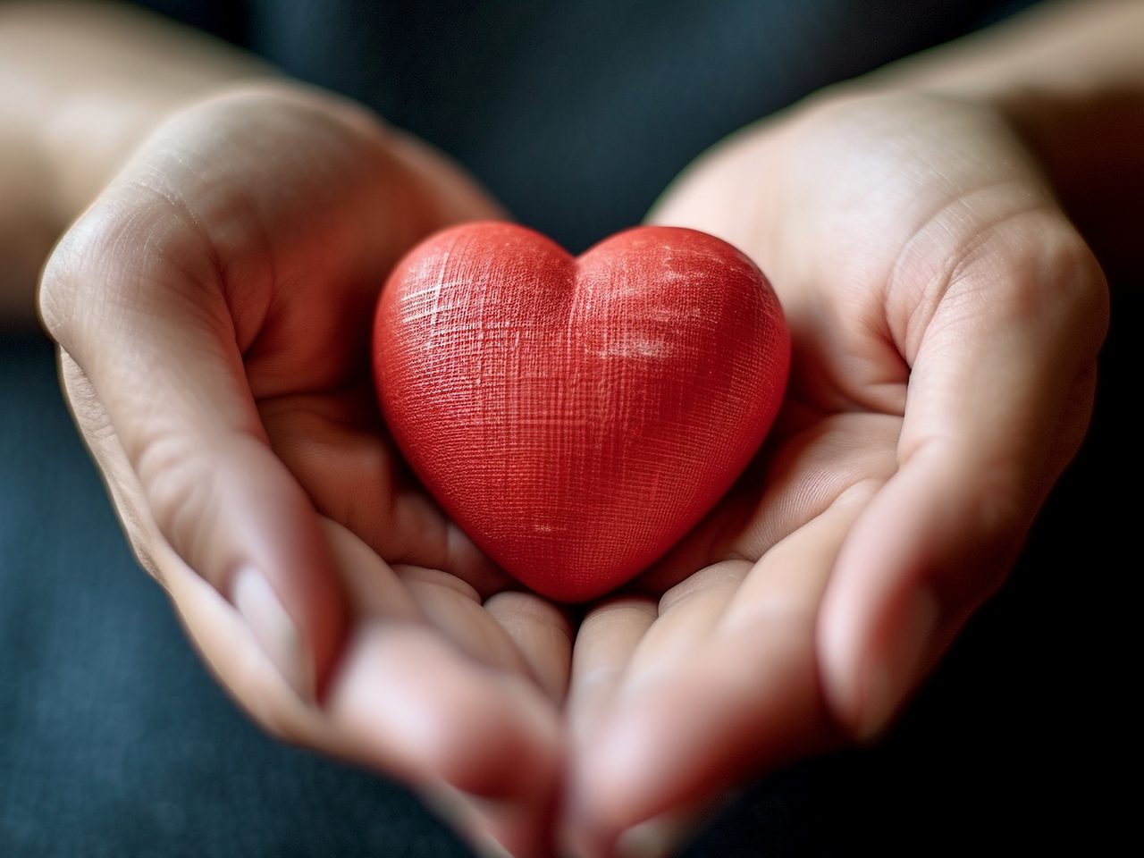 Hands holding a red heart-shaped object against a dark background.