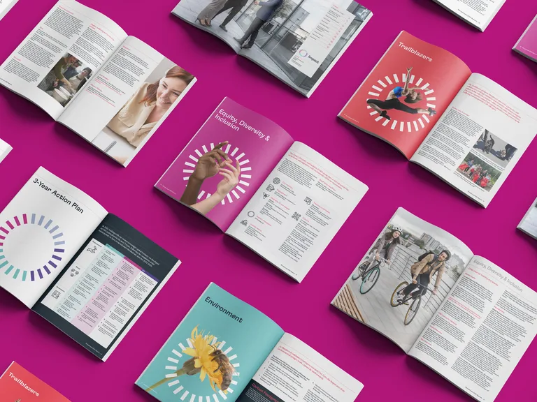 Open magazines with colorful pages and images related to diversity, environment, and action plans, laid out on a vibrant pink background.