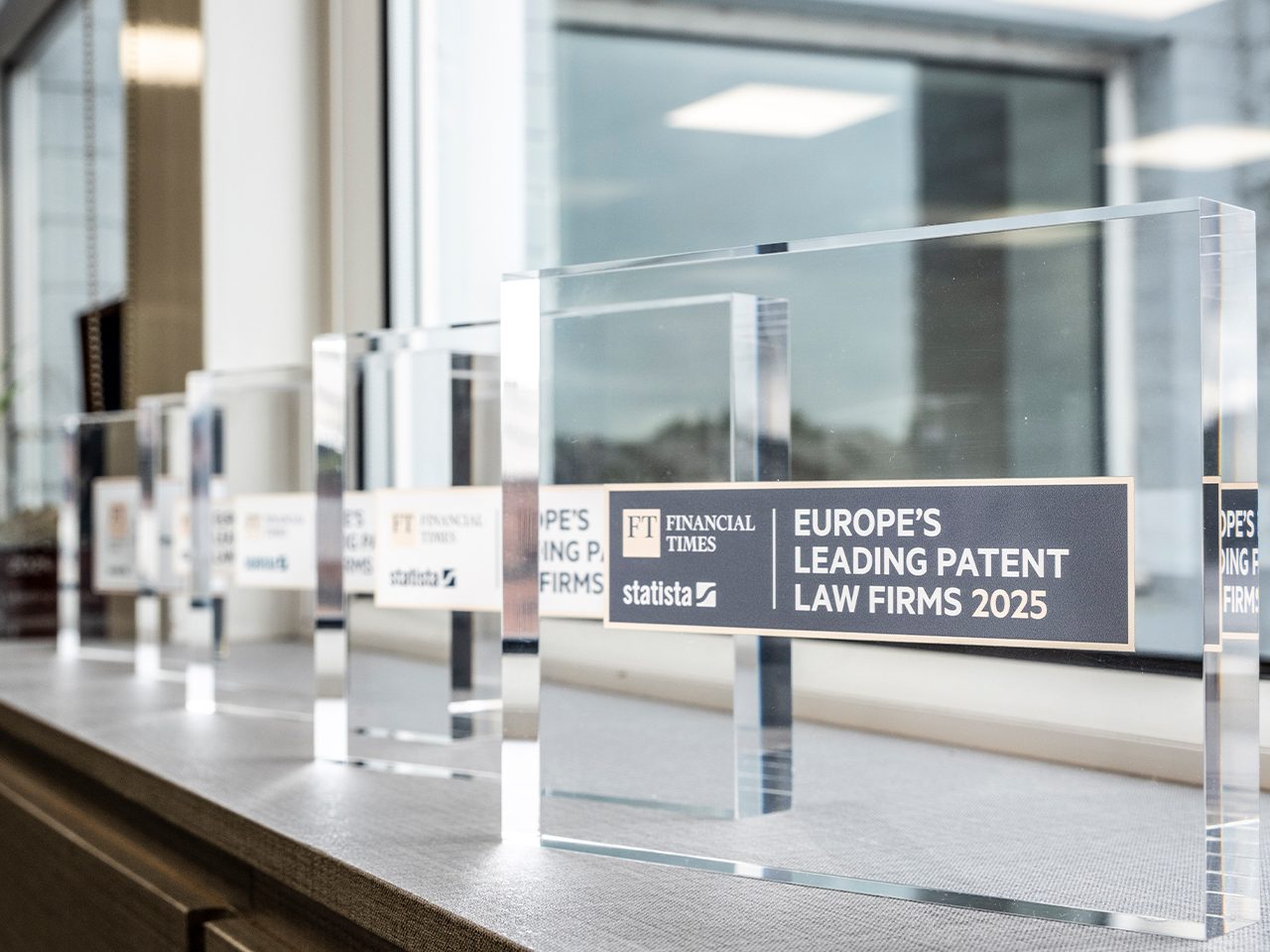 Row of clear acrylic awards on a windowsill; the front plaque reads "Europe's Leading Patent Law Firms 2025" with FT Financial Times and Statista logos.