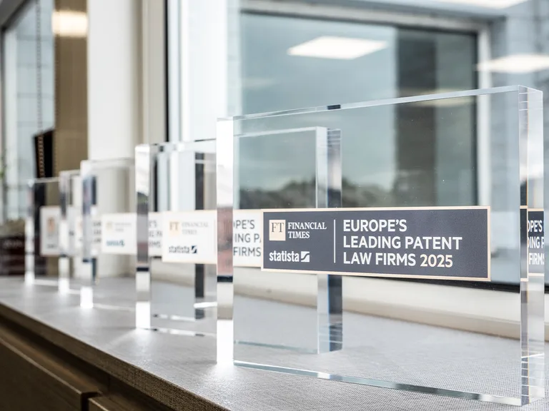 Row of clear acrylic awards on a windowsill; the front plaque reads "Europe's Leading Patent Law Firms 2025" with FT Financial Times and Statista logos.