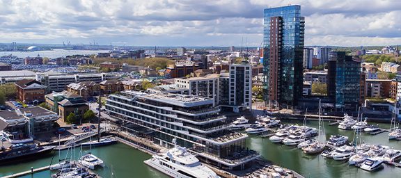 Aerial view of a city harbor with modern buildings, high-rise apartments, and boats docked along the waterfront.