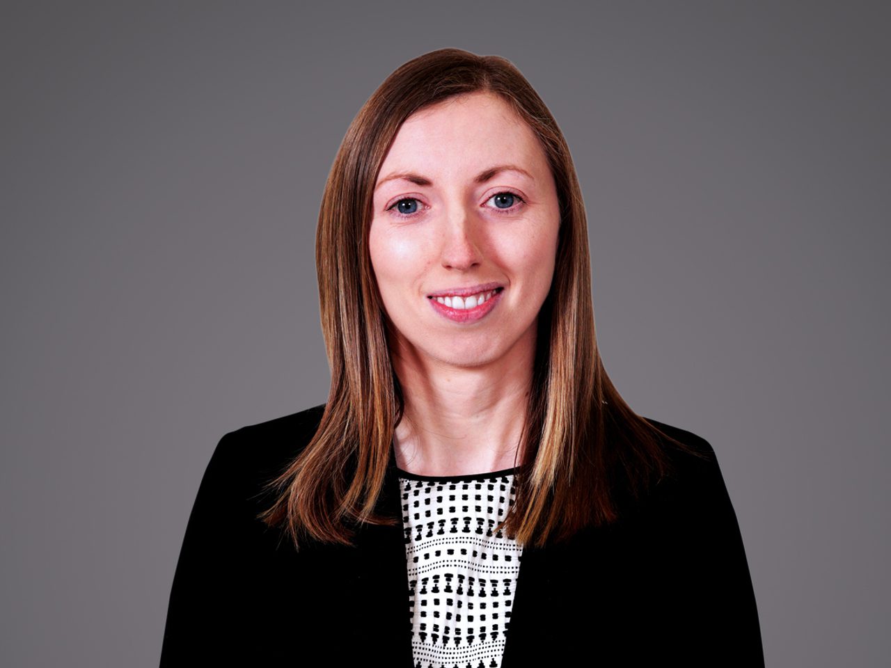 Portrait of a person with shoulder-length light brown hair, wearing a black blazer over a white and black patterned top, smiling.