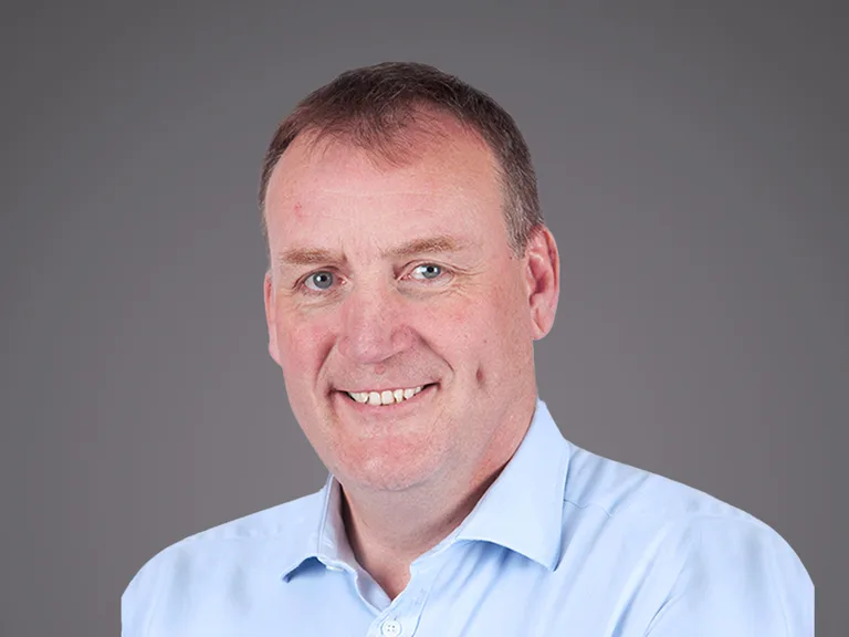 Portrait d'une personne souriante, chemise bleu clair, cheveux courts, sur fond gris dégradé.