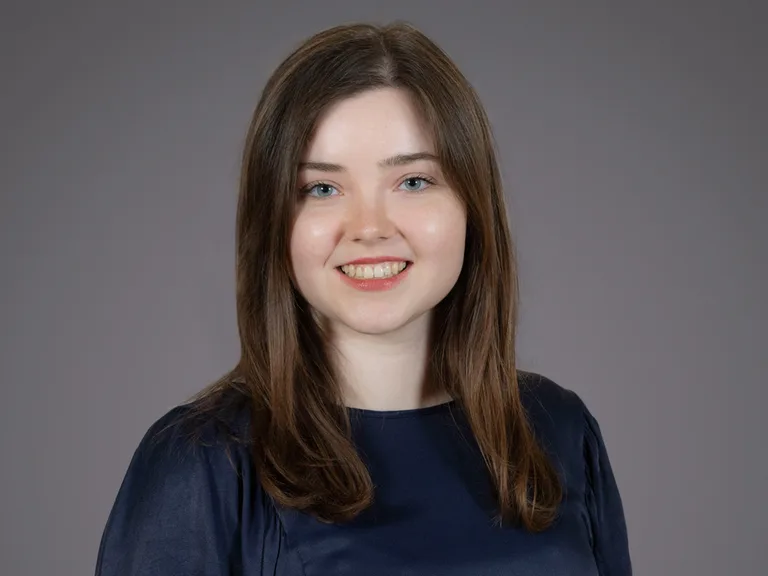 donna con capelli marroni, sorriso, vestita di blu, sfondo grigio, primo piano.