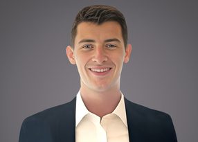 Smiling person with short dark hair wearing a dark blazer and white shirt, facing the camera against a neutral gray gradient background.