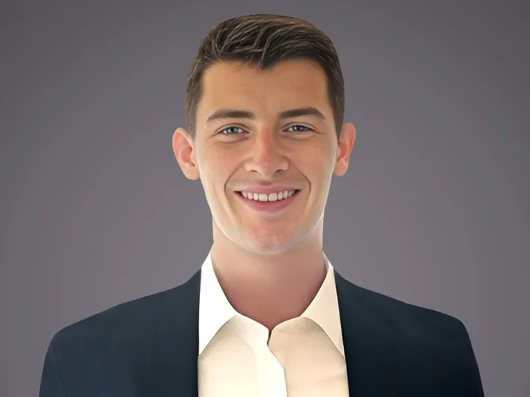 Portrait of a person with short dark hair, wearing a dark blazer and white shirt, smiling against a grey gradient background.