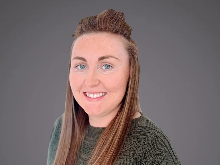 Portrait of a person with long light brown hair, blue eyes and a friendly smile, wearing a green textured knit top, against a grey gradient background.
