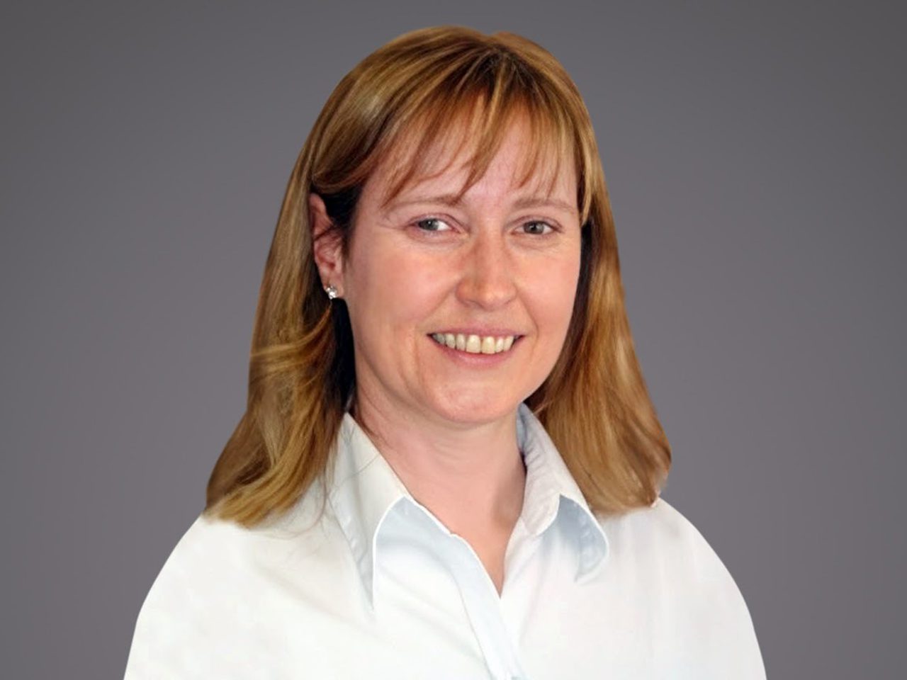 Person with shoulder-length light brown hair wearing a white button-up shirt, smiling against a neutral gray gradient background.