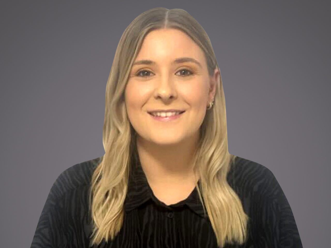 Smiling person with shoulder-length blond hair wearing a black top, against a neutral grey backdrop.