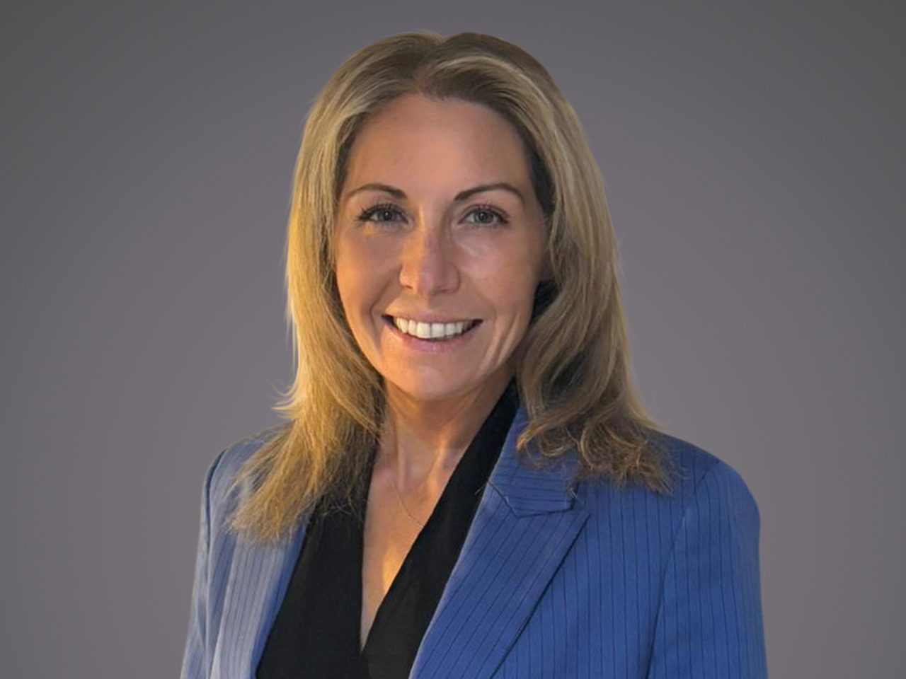 Portrait of a person with shoulder-length blonde hair, wearing a blue pinstripe blazer over a black blouse, smiling against a grey background.