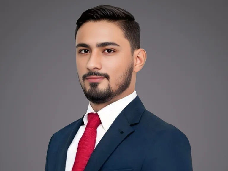 Ritratto professionale di una persona in completo blu, camicia bianca e cravatta rossa, con capelli corti e barba curata, sfondo grigio uniforme.