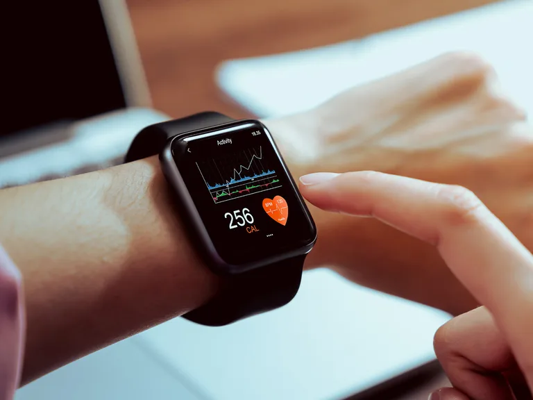 Close-up of a smartwatch on a wrist showing an activity graph and 256 CAL, with a heart-rate icon, as a finger taps the screen.