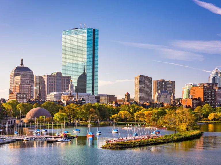 City skyline with modern skyscrapers, a park with sailboats in the water, and a clear blue sky in the background.