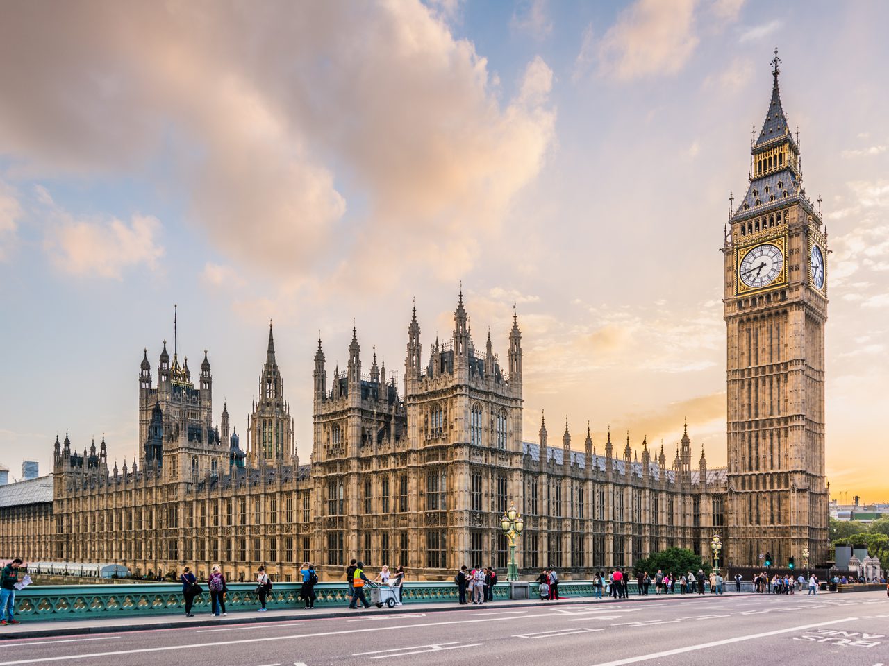 Big Ben and the Palace of Westminster at sunset with people walking on the bridge in the foreground.