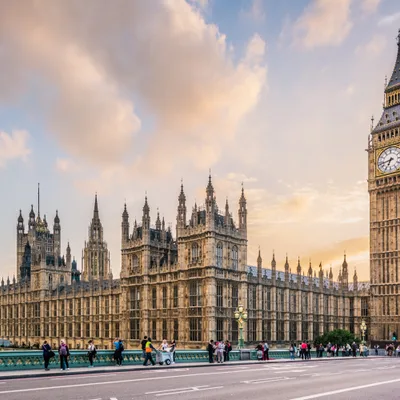 Big Ben and the Palace of Westminster at sunset with people walking on the bridge in the foreground.