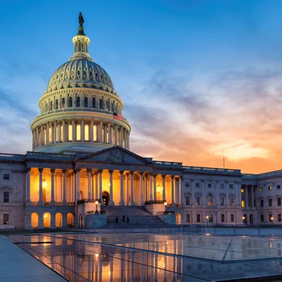 The United States Capitol building at sunset with clouds in the sky and lights illuminating the structure.