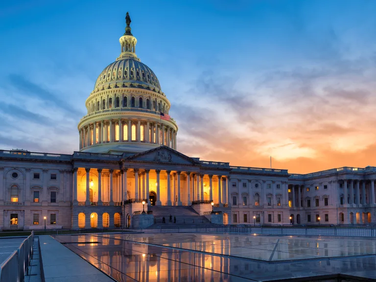 The United States Capitol building at sunset with clouds in the sky and lights illuminating the structure.