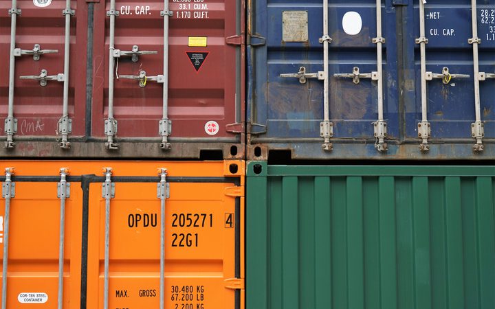 Close-up of four stacked shipping containers in red, blue, orange, and green, showcasing locked doors, identification markings, and industrial details.