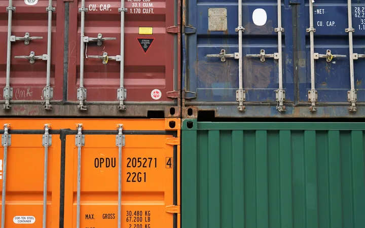 Close-up of four stacked shipping containers in red, blue, orange, and green, showcasing locked doors, identification markings, and industrial details.