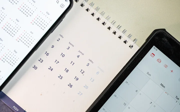 Three devices on a beige surface showing calendars: a left smartphone with a yearly calendar, a middle spiral notebook calendar, and a right device with a calendar app.
