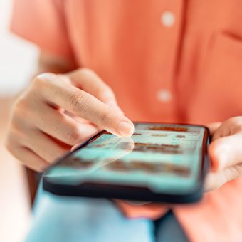 Close-up of a person in an orange shirt tapping app icons on a touchscreen smartphone.