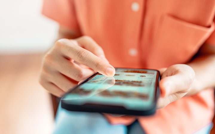 Close-up of a person in an orange shirt tapping app icons on a touchscreen smartphone.