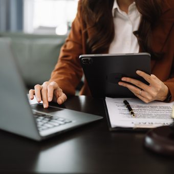 Portrait of a person with short light-brown hair and a light beard, in a dark grey blazer and a white dotted shirt, smiling against a grey backdrop.