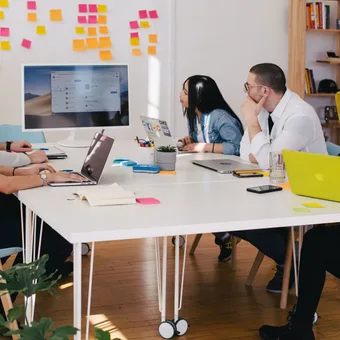 Five people sitting around a conference table in an office, facing a large monitor, engaged in a discussion or presentation.