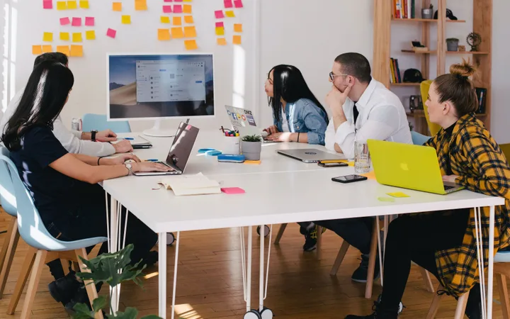 Five people sitting around a conference table in an office, facing a large monitor, engaged in a discussion or presentation.