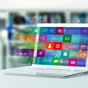 A white laptop displaying a colourful interface with various icons and digital elements, set against a blurred background.