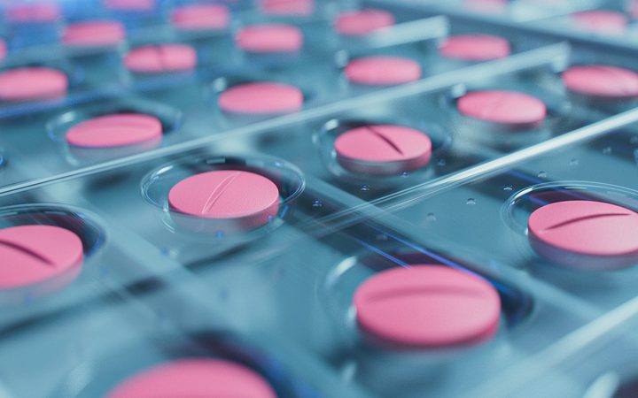 Close-up of pink round tablets in blister packs, arranged neatly in a grid, with some pills partially out of focus in the background.
