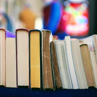 A row of worn and colourful books standing on a black surface with a blurred colorful background.