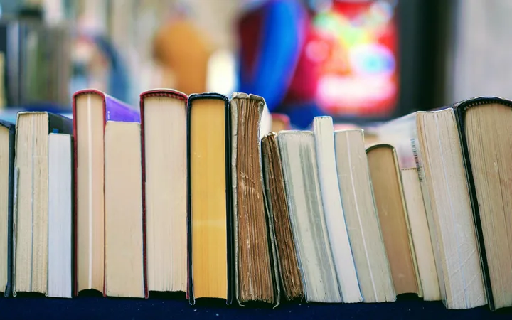 A row of worn and colourful books standing on a black surface with a blurred colorful background.