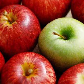 A close-up of a group of red apples with one bright green apple in the centre, all arranged on a wooden surface.