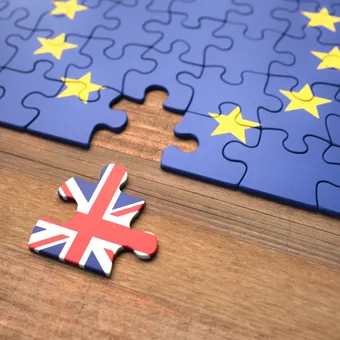 Blue EU flag puzzle on a wooden table with a lone UK flag piece nearby.