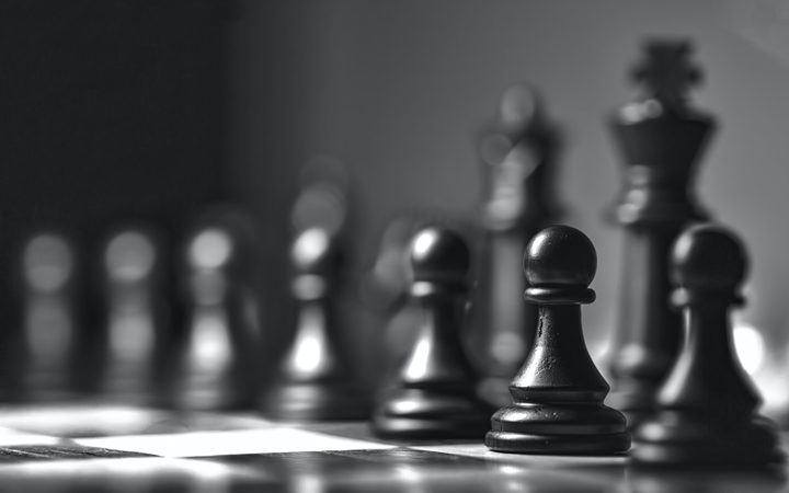 Black and white close-up of a chessboard with pawns in focus and a king in the background, indicating an intense game scene.