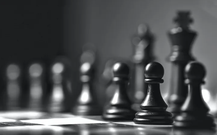 Black and white close-up of a chessboard with pawns in focus and a king in the background, indicating an intense game scene.