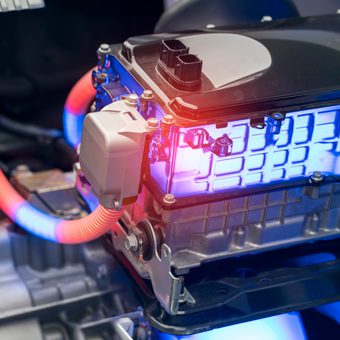 Close-up of an electric car motor with bright blue lighting, orange and blue wiring, and various metal and plastic components in a vehicle interior.