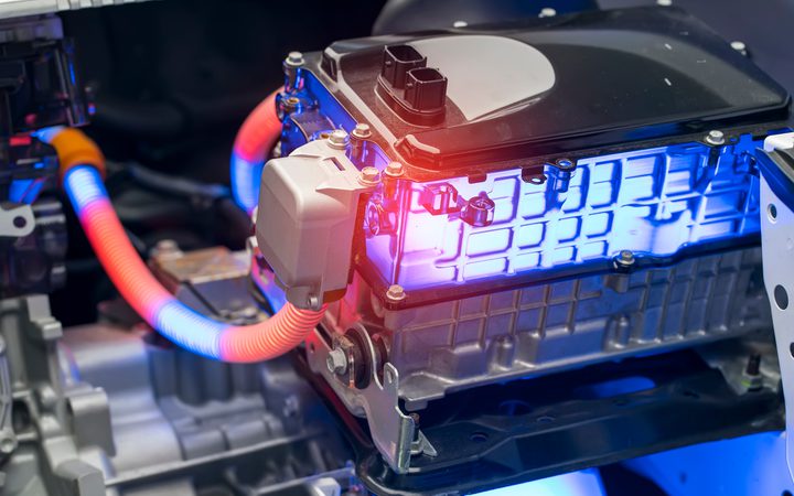 Close-up of an electric car motor with bright blue lighting, orange and blue wiring, and various metal and plastic components in a vehicle interior.