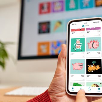 Portrait of a person with long dark hair, round glasses, and a green textured top, smiling softly against a grey studio backdrop.