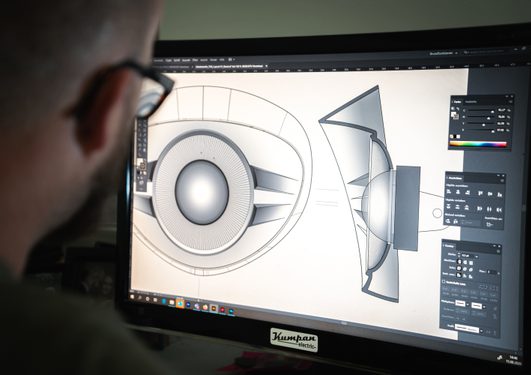 Person betrachtet einen Monitor mit technischer 3D-Designzeichnung eines Lautsprechers, auf dem verschiedene Gestaltungselemente sichtbar sind.