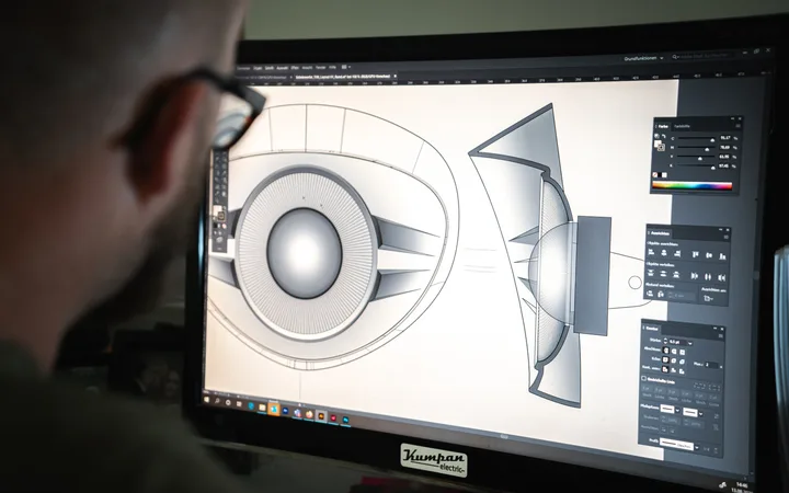 Person betrachtet einen Monitor mit technischer 3D-Designzeichnung eines Lautsprechers, auf dem verschiedene Gestaltungselemente sichtbar sind.