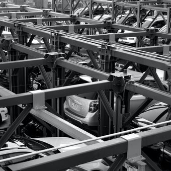 Multi-storey car park with cars on automated lifts, showing a complex steel framework structure in black and white.