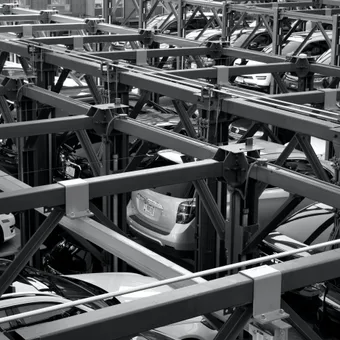 Multi-storey car park with cars on automated lifts, showing a complex steel framework structure in black and white.