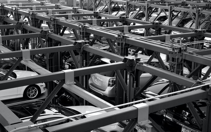 Multi-storey car park with cars on automated lifts, showing a complex steel framework structure in black and white.