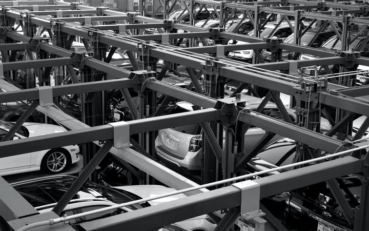 Multi-storey car park with cars on automated lifts, showing a complex steel framework structure in black and white.