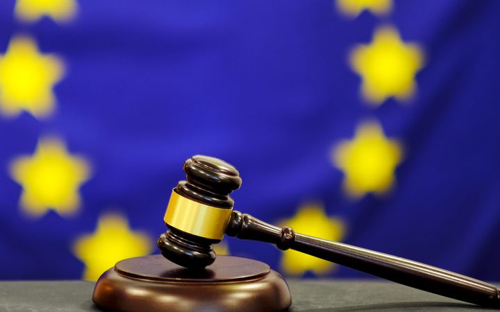 Gavel resting on a sound block with a blurred European Union flag background featuring yellow stars on a blue field.