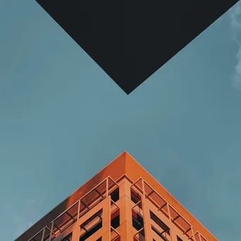 Low-angle view of an orange building with balconies against a blue sky with scattered clouds. A black triangular shape is in the foreground.