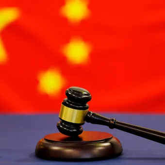 A judge's gavel resting on a table with the Chinese flag blurred in the background.
