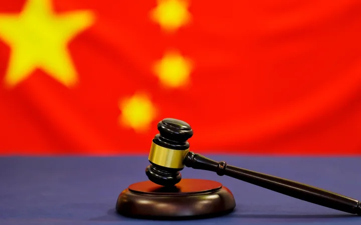 A judge's gavel resting on a table with the Chinese flag blurred in the background.